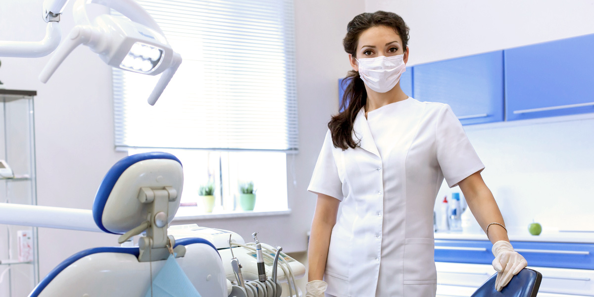 A dental assistant wearing their uniform and standing in a dentist’s office