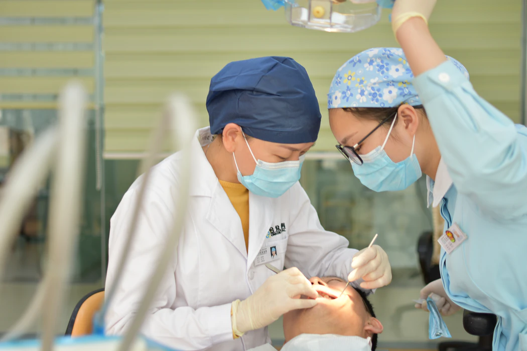 A dentist performing teeth cleaning with the aid of a dental assistant
