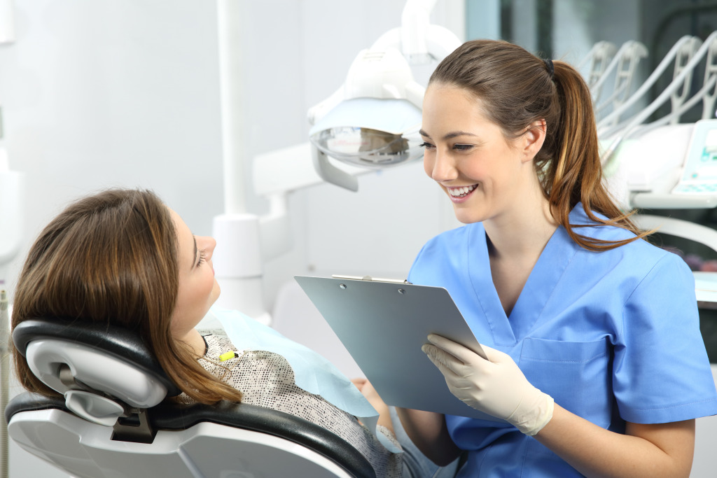 A person in blue scrubs holding a clipboard and looking at a patient