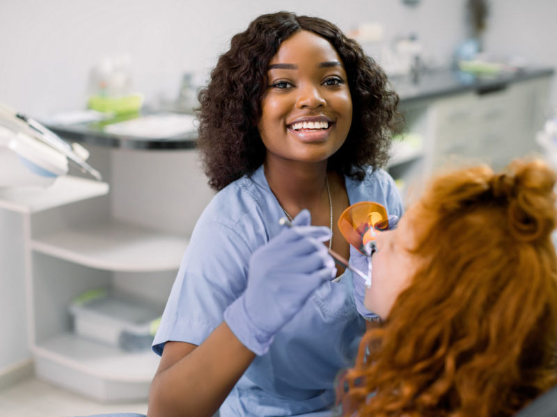 Smiling,Black,Woman,Dentist,Wearing,Blue,Uniform,,Providing,Tooth,Restoration