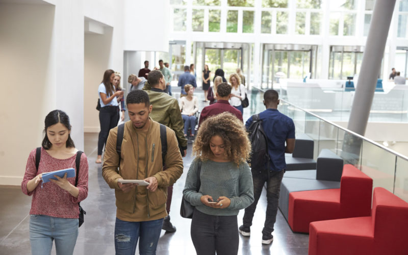 Students,Walk,In,University,Campus,Using,Tablets,And,Phone