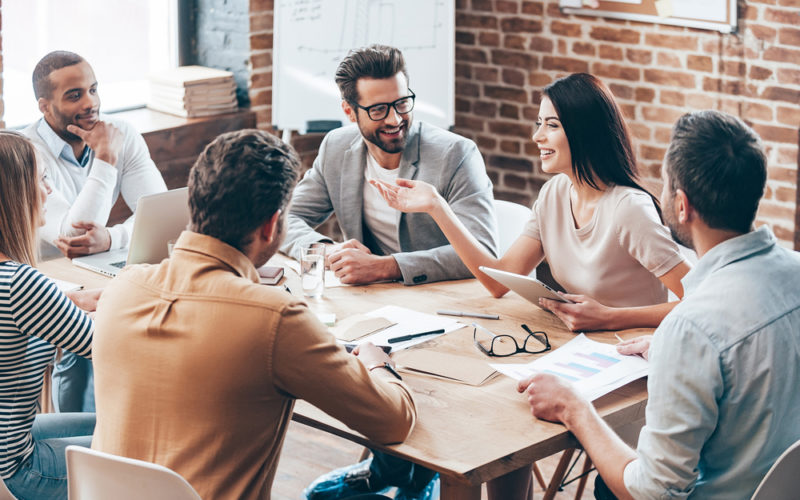 Making great decisions. Young beautiful woman gesturing and discussing something with smile while her coworkers listening to her sitting at the office table